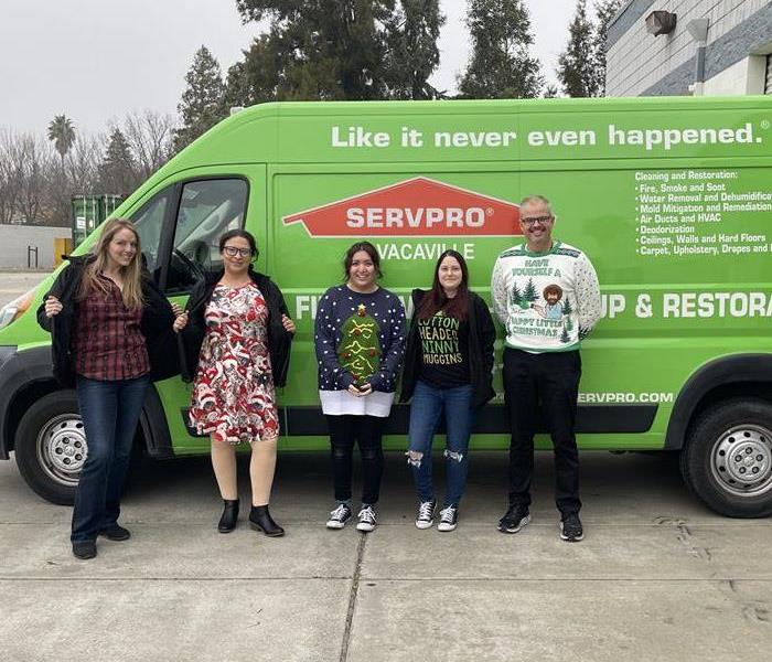 Image shows employees dressed in ugly Christmas sweaters posing in front of a SERVPRO vehicle